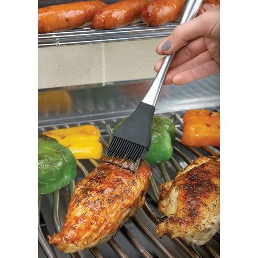 Woman basting a chicken breast on a grill with a silicone brush