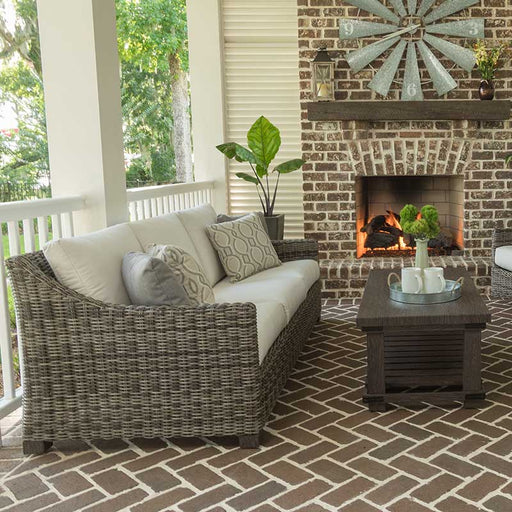 Woven outdoor sofa on a covered patio next to a fire place